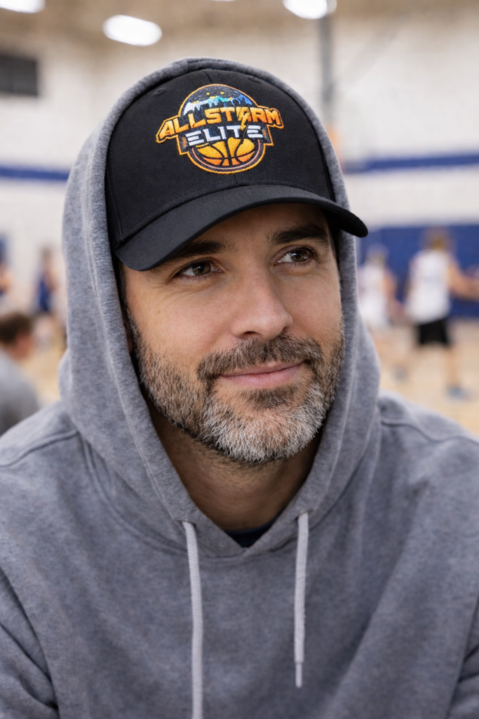 Parent wearing AllStorm Elite black embroidered baseball cap at youth basketball game